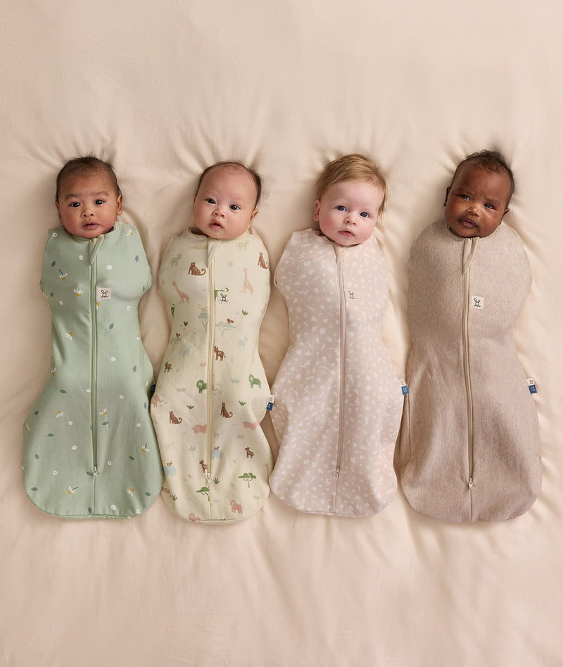 Four babies lying on a cream blanket wearing ergoPouch Cocoon Swaddle Bags  in Meadow, Savannah, Coastal, and Taupe Marle