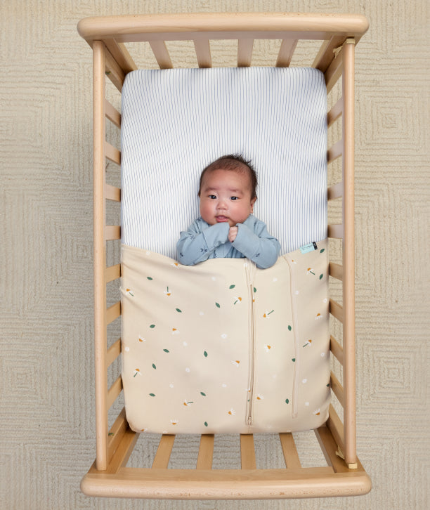 Baby tucked in a bassinet with the HugMe Blanket