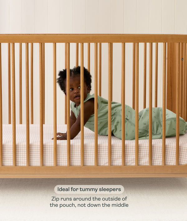 Product feature graphic showing a baby on their stomach in a green Sleeping Bag, with text explaining the side-zip feature for tummy sleepers.