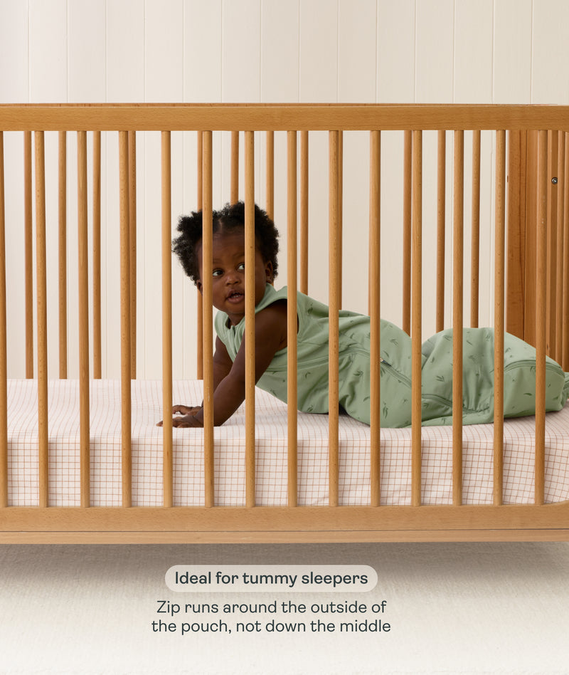Product feature graphic showing a baby on their stomach in a green Sleeping Bag, with text explaining the side-zip feature for tummy sleepers.