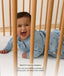 Baby lying on their tummy in a wooden cot wearing a blue long sleeved Sleeping Bag, with text noting it is ideal for tummy sleepers.