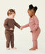 Two toddlers standing and holding hands, wearing long-sleeve pyjama sets with matching pants—one in brown and one in dusty pink—designed for comfort and movement.