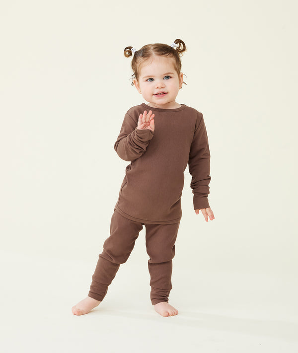 Toddler standing against a cream background wearing a brown long-sleeve pyjama set with matching pants, shown in a relaxed pose.