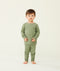 Toddler standing against a  cream background wearing an olive green long-sleeve pyjama set with matching pants, made from soft, comfortable fabric.