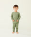 Toddler standing against a  cream background wearing an olive green long-sleeve pyjama set with matching pants, made from soft, comfortable fabric.