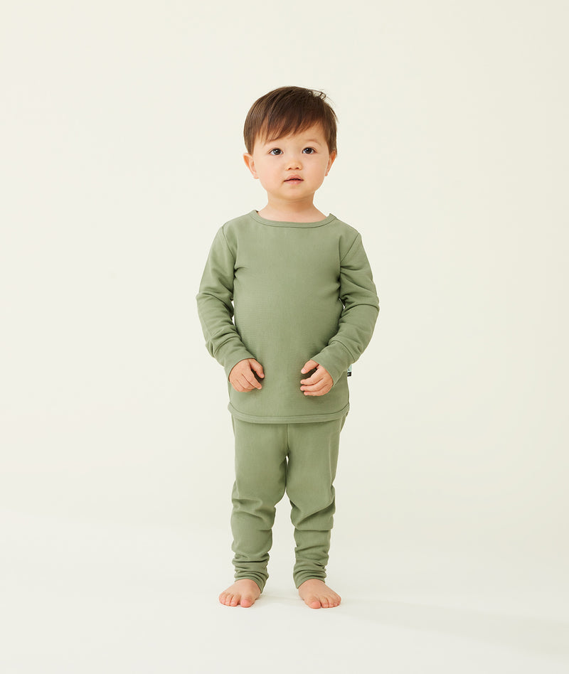 Toddler standing against a  cream background wearing an olive green long-sleeve pyjama set with matching pants, made from soft, comfortable fabric.
