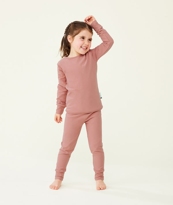 A happy little girl wearing a blush pink Long Sleeve Pyjama Set with matching pants, made from soft, comfortable fabric.