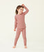 A happy little girl wearing a blush pink Long Sleeve Pyjama Set with matching pants, made from soft, comfortable fabric.