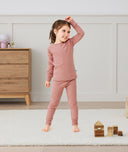 A happy little girl wearing a blush pink Long Sleeve Pyjama Set with matching pants, made from soft, comfortable fabric.