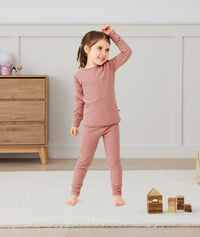 A happy little girl wearing a blush pink Long Sleeve Pyjama Set with matching pants, made from soft, comfortable fabric.