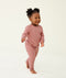 Toddler walking barefoot on a cream background wearing a blush pink long-sleeve pyjama set with matching pants, made from soft, comfortable fabric.