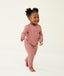 Toddler walking barefoot on a cream background wearing a blush pink long-sleeve pyjama set with matching pants, made from soft, comfortable fabric.