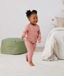 Toddler walking inside the bedroom wearing a blush pink long-sleeve pyjama set with matching pants, made from soft, comfortable fabric.