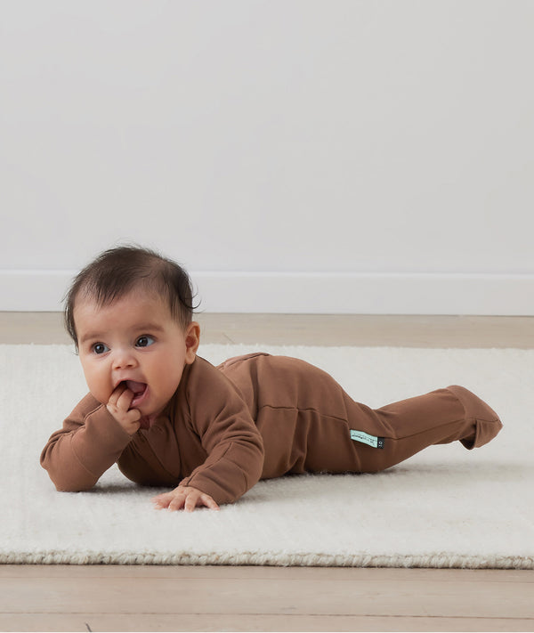 Baby lying on its tummy wearing an ergoPouch Long Sleeve Layer, featuring slim-fit design and fold over hand and foot cuffs. 
