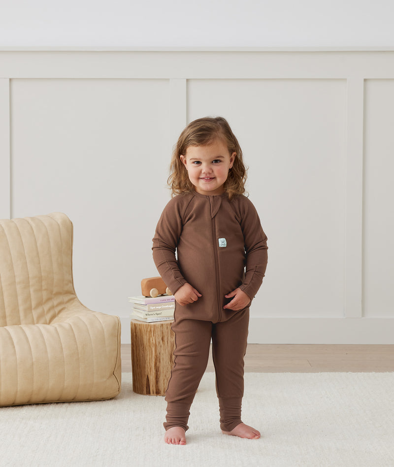 Toddler standing indoors wearing a brown Long Sleeve Layer by ergroPouch, featuring slim-fit design and front zipper.