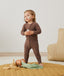 Toddler standing indoors wearing a brown long-sleeve zip-front base layer, designed for a close, comfortable fit.
