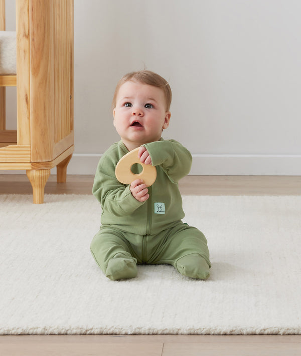 Infant sitting upright wearing an olive green Long Sleeve Layer by ergoPouch, featuring front-zip design and fold over hand and foot cuffs.
