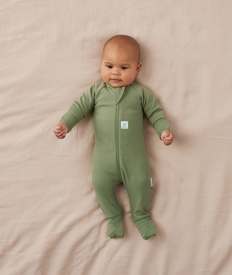 Baby lying on a beige blanket wearing a slim-fit Long Sleeve Layer by ergoPouch, featuring fold over hand and foot cuffs.