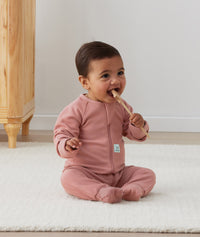 Infant sitting on a rug wearing a Long Sleeve Layer with its foot cuffs folded over.
