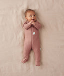 Baby lying on a beige blanket wearing an ergoPouch Long Sleeve Layer in Rose, featuring fold over foot cuffs.