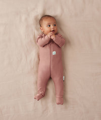 Baby lying on a beige blanket wearing an ergoPouch Long Sleeve Layer in Rose, featuring fold over foot cuffs.