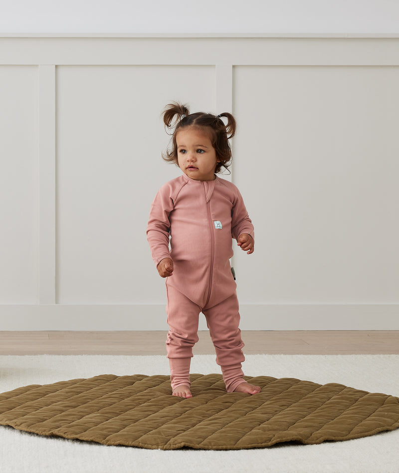 Toddler standing on a rug wearing a Long Sleeve Layer 2.0 TOG Rose, featuring front zipper and soft, breathable fabric.