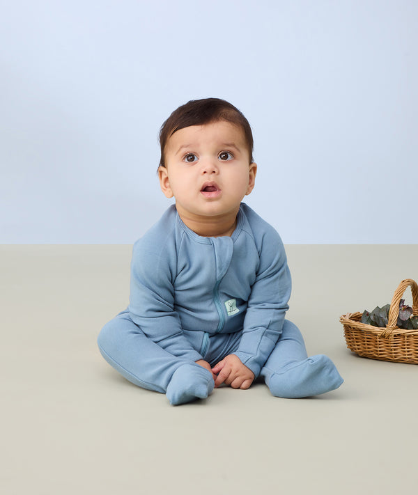Baby sitting upright wearing a light blue Long Sleeve Layer, featuring fold over foot cuffs for extra warmth and protection.