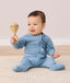 Baby sitting on a rug wearing a light blue long-sleeve zip-front pyjama set with matching pants, made from soft, comfortable fabric.