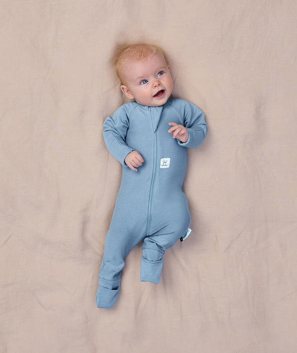 Baby lying on a beige blanket wearing a light blue Long Sleeve Layer, featuring a slim fit design.