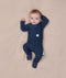 Baby lying on a beige blanket wearing a slim-fit Long Sleeve Layer by ergoPouch, featuring front-zip design and fold over cuffs.