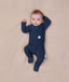Baby lying on a beige blanket wearing a slim-fit Long Sleeve Layer by ergoPouch, featuring front-zip design and fold over cuffs.