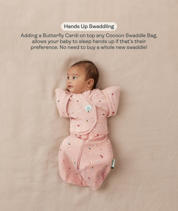 Baby lying on their back in a pink floral-patterned Cocoon Swaddle Bag with a matching Butterfly Cardi, enabling hands-up swaddled sleeping.
