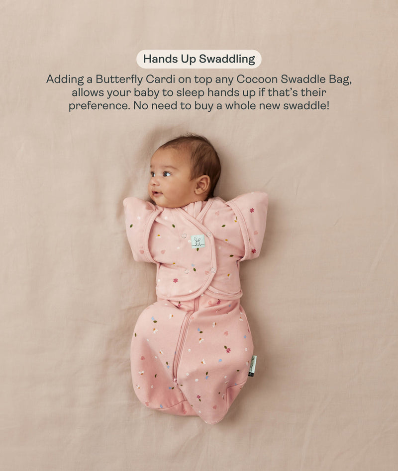 Baby lying on their back in a pink floral-patterned Cocoon Swaddle Bag with a matching Butterfly Cardi, enabling hands-up swaddled sleeping.