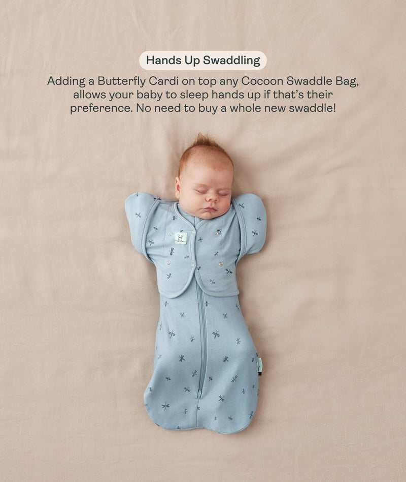 Baby lying on their back in a blue dragonfly-patterned Cocoon Swaddle Bag with a matching Butterfly Cardi, enabling hands-up swaddled sleeping.