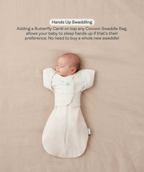 Sleeping baby lying on their back in a cream Cocoon Swaddle Bag with a matching Butterfly Cardi, enabling hands-up swaddled sleeping.