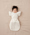 Baby lying on their back wearing a Cocoon Swaddle Bag with Butterfly Cardi over top for hands up sleeping.