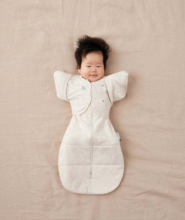 Baby lying on their back wearing a Cocoon Swaddle Bag with Butterfly Cardi over top for hands up sleeping.
