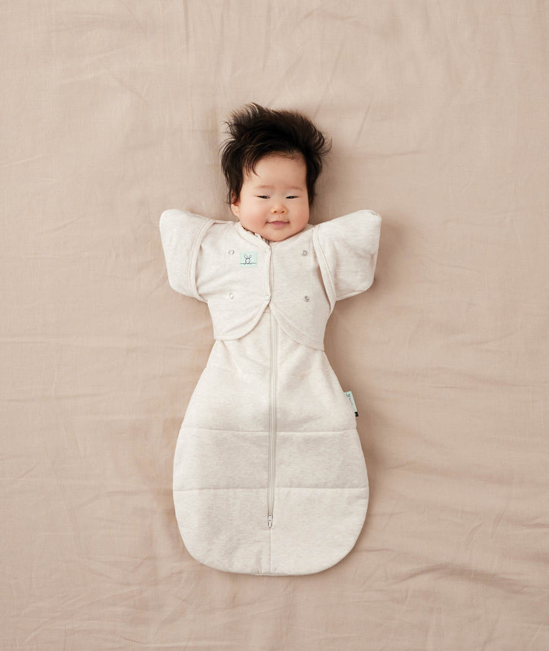 Baby lying on their back wearing a Cocoon Swaddle Bag with Butterfly Cardi over top for hands up sleeping.