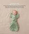 Baby lying on their back in a green leaf-patterned Cocoon Swaddle Bag with a matching Butterfly Cardi, enabling hands-up swaddled sleeping.