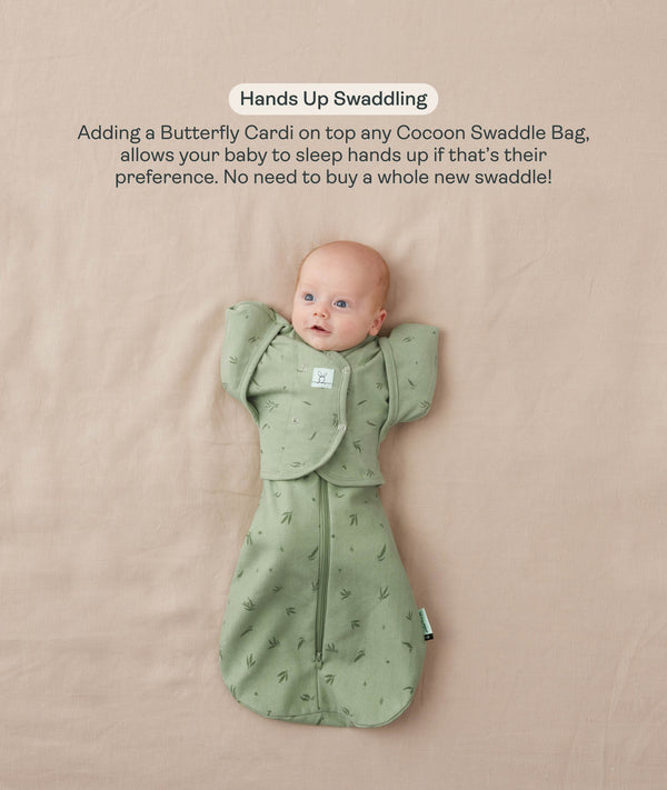 Baby lying on their back in a green leaf-patterned Cocoon Swaddle Bag with a matching Butterfly Cardi, enabling hands-up swaddled sleeping.