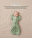 Baby lying on their back in a green leaf-patterned Cocoon Swaddle Bag with a matching Butterfly Cardi, enabling hands-up swaddled sleeping.