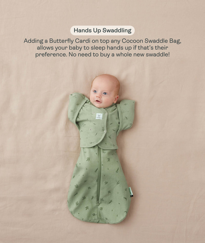 Baby lying on their back in a green leaf-patterned Cocoon Swaddle Bag with a matching Butterfly Cardi, enabling hands-up swaddled sleeping.