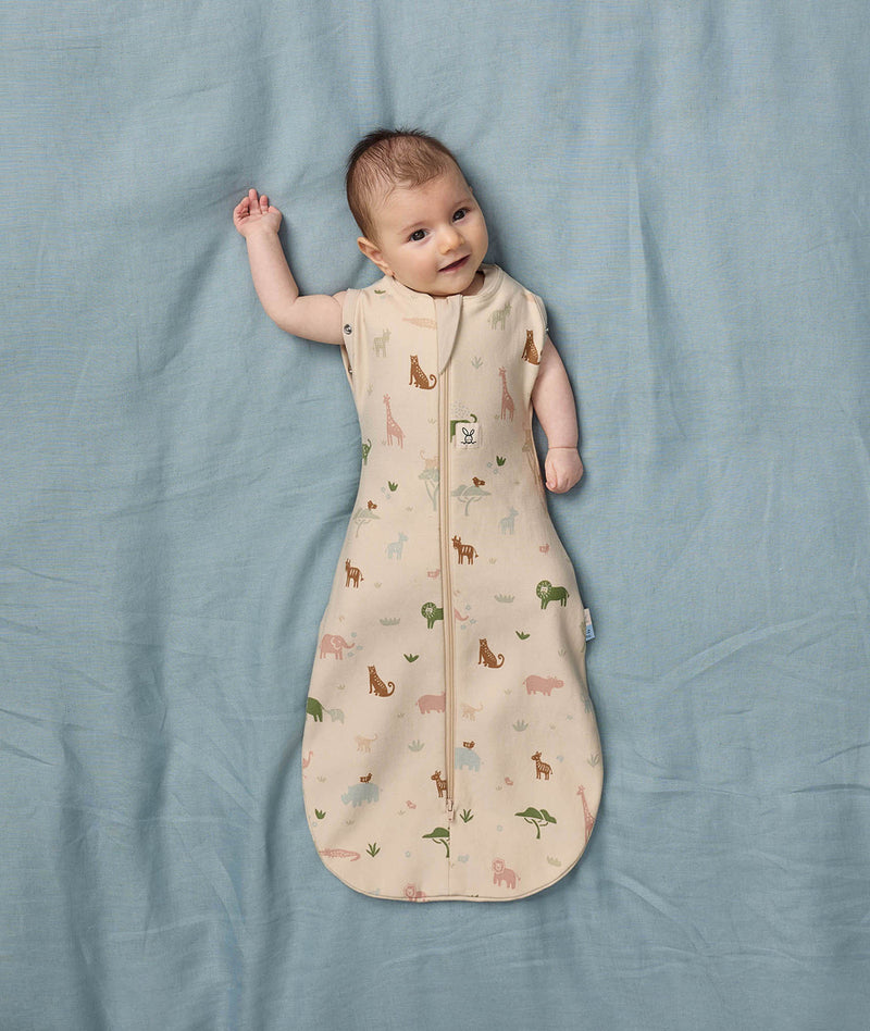 Baby lying on a soft blue sheet wearing a Safari-themed Cocoon Swaddle Bag with its arms outside.