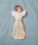 A bay lies on s soft blue sheet wearing a Cocoon Swaddle Bag with Butterfly Cardi to keep its arms secure in a raised position.