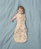 A baby lies on a blue surface wearing a Cocoon Swaddle Bag with colourful Safari animal prints.
