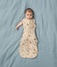 A baby lies on a blue surface wearing a Cocoon Swaddle Bag with colourful Safari animal prints.