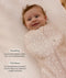 Smiling baby wrapped in a Cocoon Swaddle Bag lying on a grid-patterned sheet with text highlighting  swaddling benefit and TOG rating feature.
