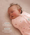 Close-up view of a sleeping baby being swaddled in a pink floral Cocoon Swaddle Bag with text highlighting swaddling benefit and TOG rating feature.