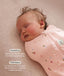 Close-up view of a sleeping baby being swaddled in a pink floral Cocoon Swaddle Bag with text highlighting swaddling benefit and TOG rating feature.