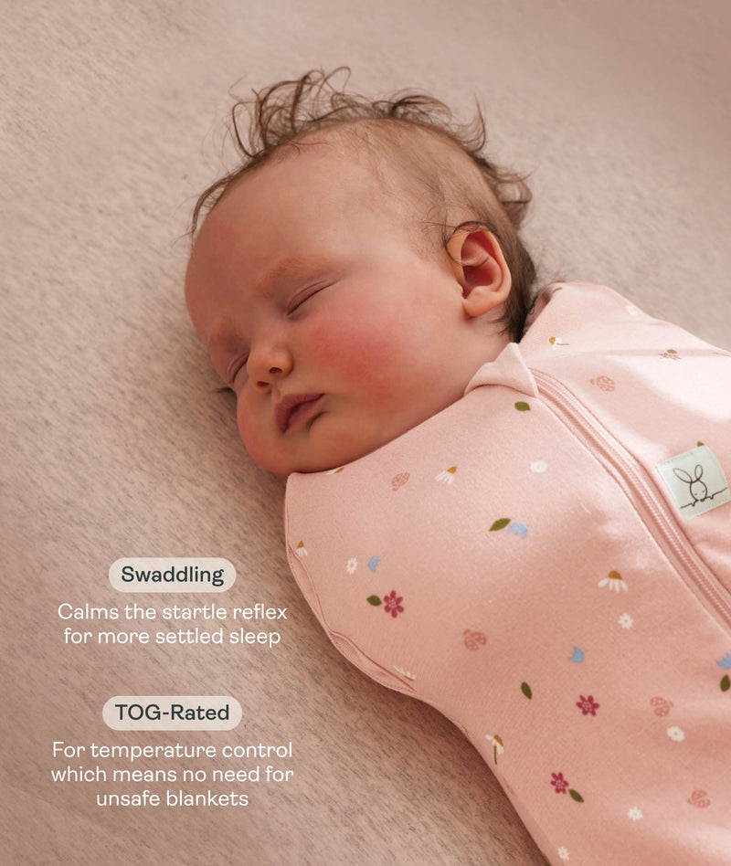 Close-up view of a sleeping baby being swaddled in a pink floral Cocoon Swaddle Bag with text highlighting swaddling benefit and TOG rating feature.